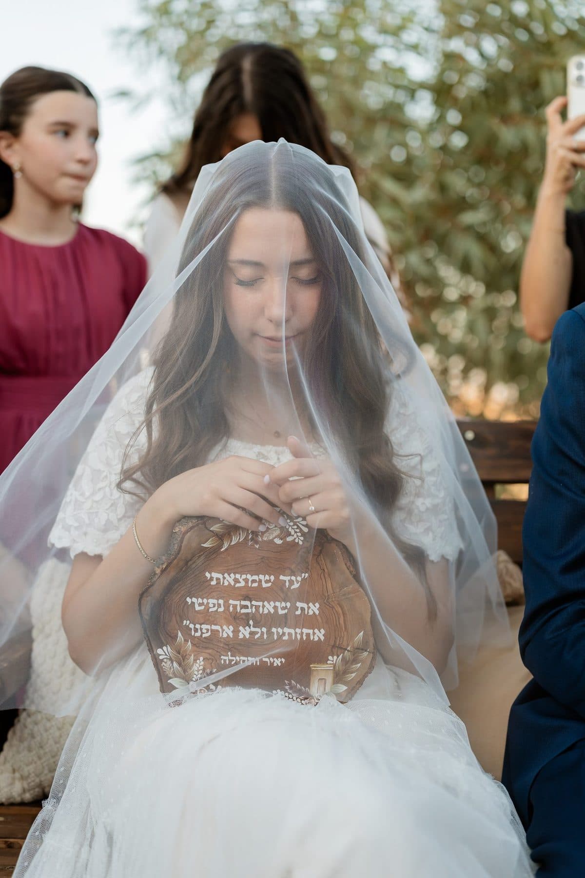כלה עם הינומה מביטה למטה ומחזיקה שלט מעוצב עם ברכה